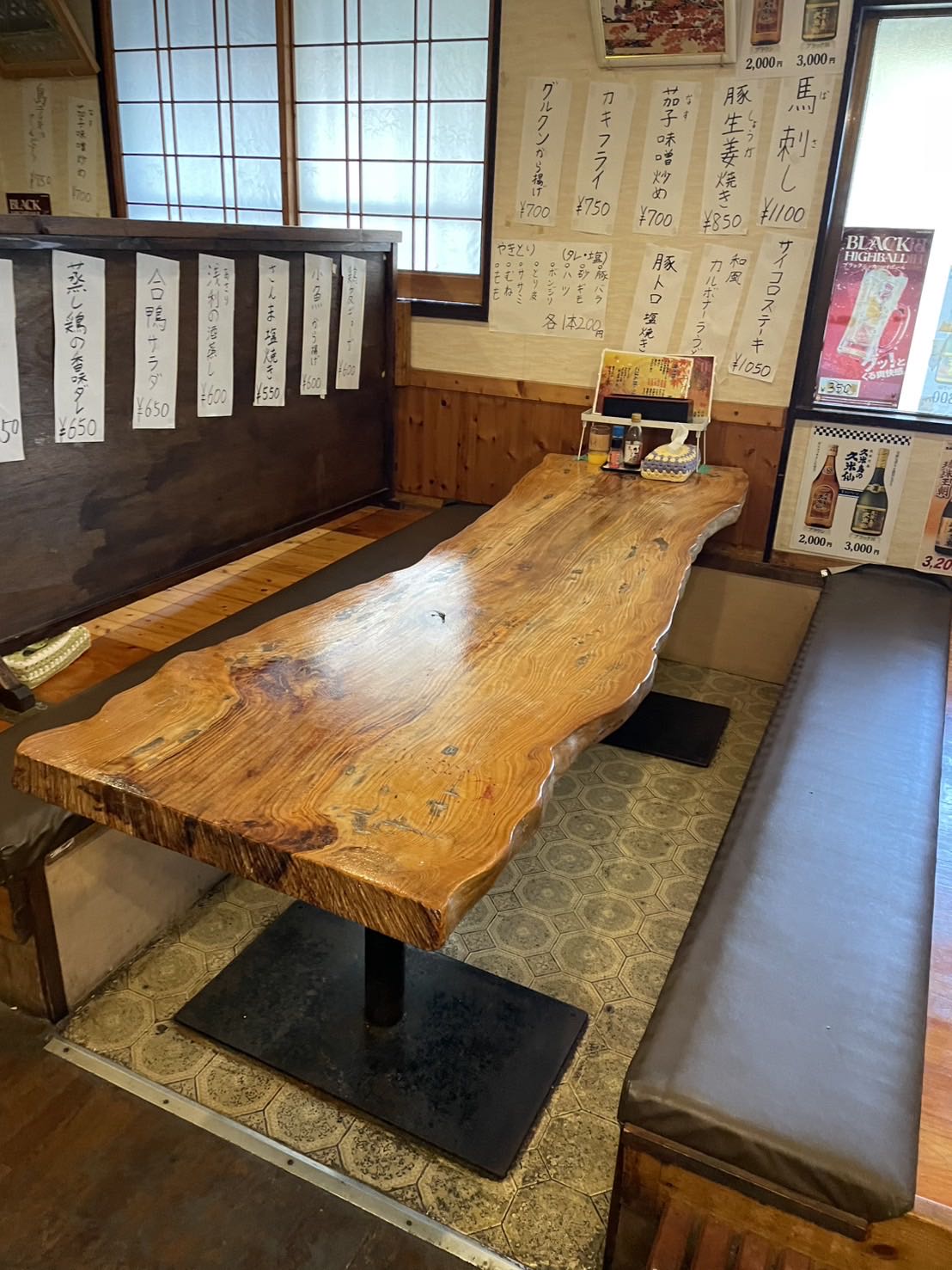 花いちのテーブル席。一枚板の大きなテーブルと、壁一面の手書きのお品書き